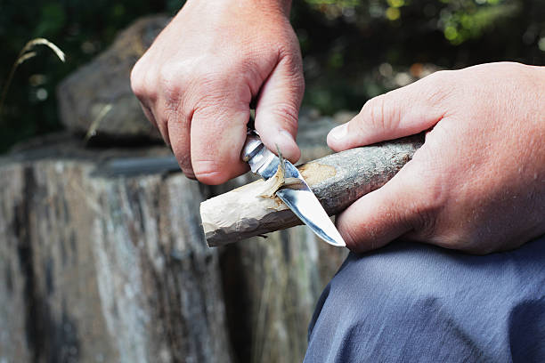 A man uses a palm knife with a sharp blade to carve a wooden stick.