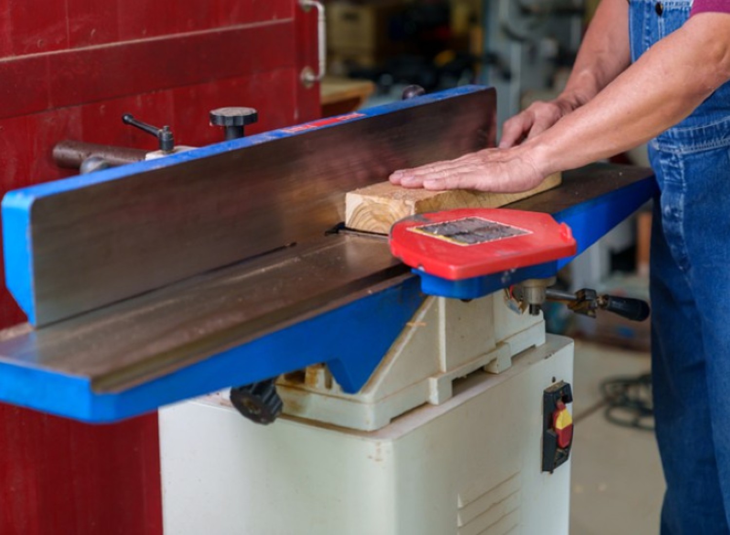 Image of a man in overalls using a cabinet table saw to cut a piece of wood.