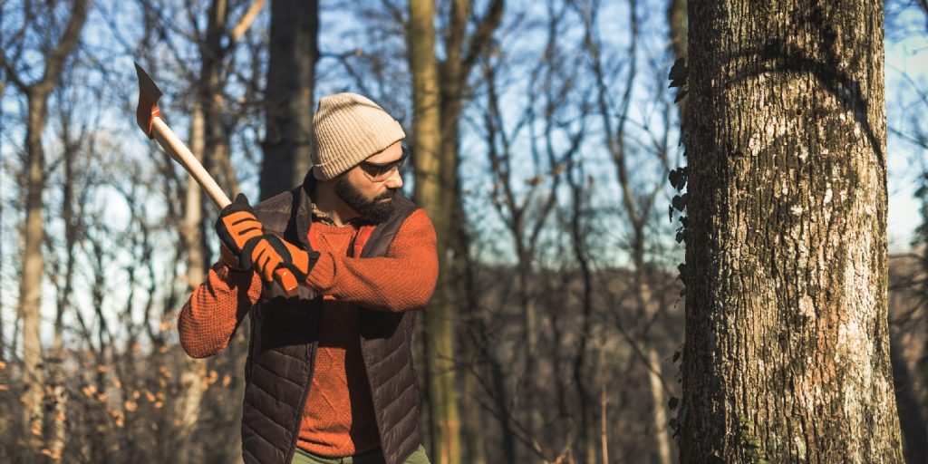 Image of one masculine man with beard in woods with work tools.
