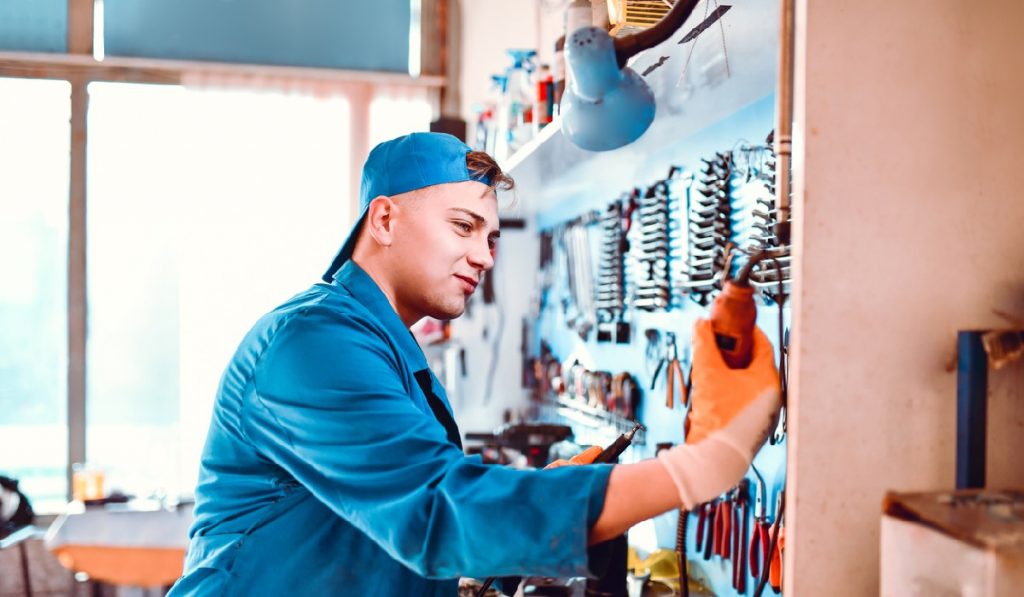 Young Mechanic Taking Wire Soldering Iron In Workshop