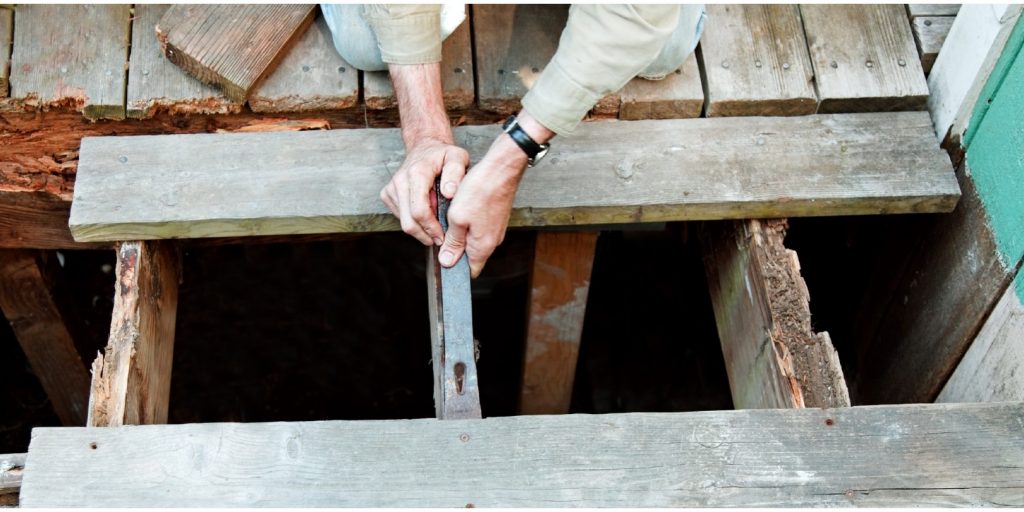 Kneeling worker prying off rotten deck planks