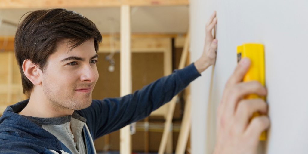 Young man with stud finder examining wall at home