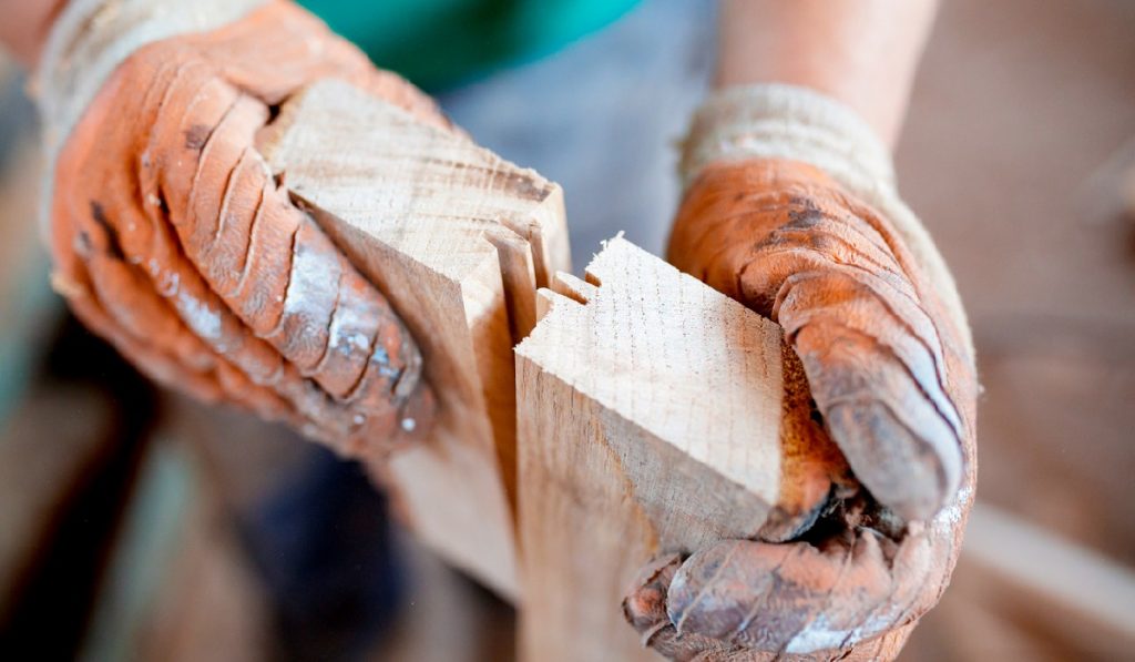 Close-up of carpenter wearing protective gloves, making sure wood joinery fits perfectly
