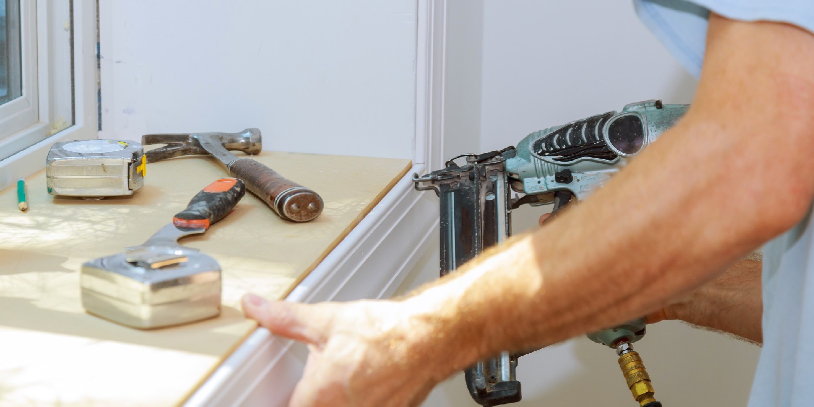 Carpenter using air nail gun to moldings for window