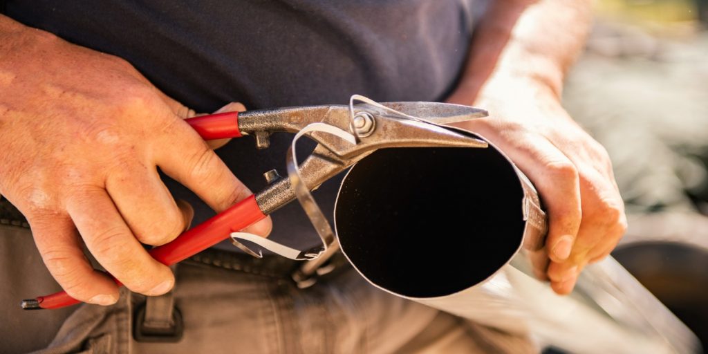 Roofer builder worker finishing folding a metal gutter using special scissors, roof gutter, close up