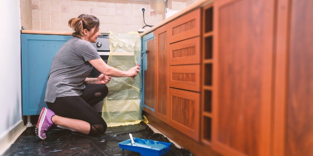 Mid age woman painting her old brown kitchen to blue modern color.