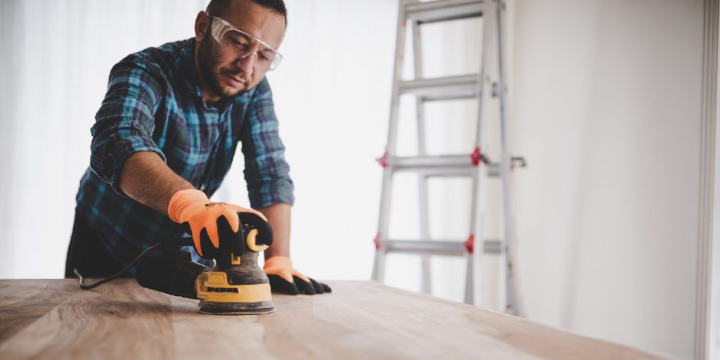 Manual worker using an electric sander to restore a wood dining table.