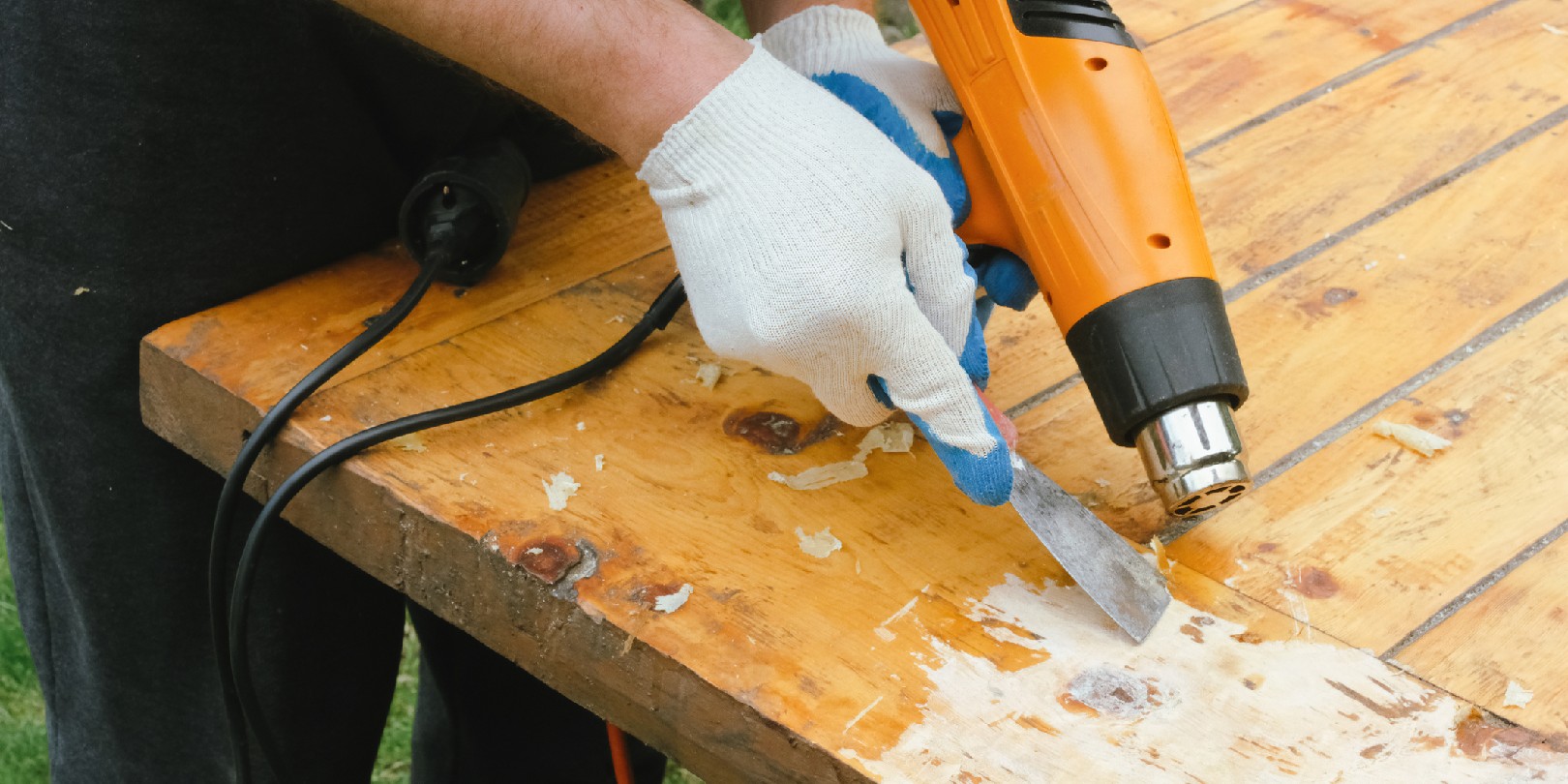 Man removing old varnish from wood using scraper and heat gun