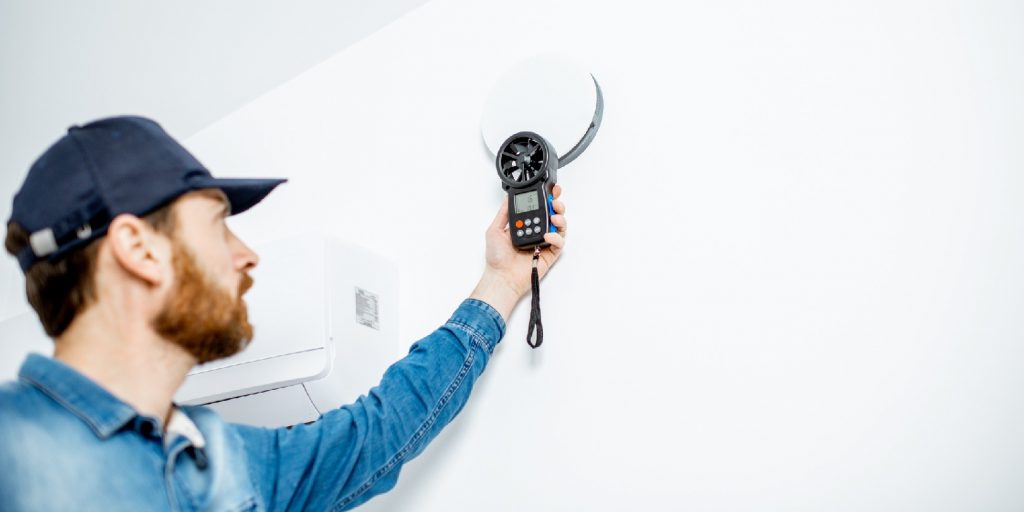 Handyman checking the speed of air ventilation with measuring tool on the white wall background