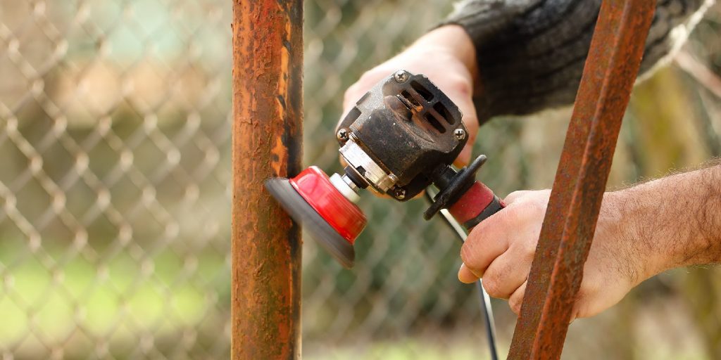 Man hands holding a working angel grinder, removing the rust from an old metal profile. Close up view of the grinding of a rusty metal construction.