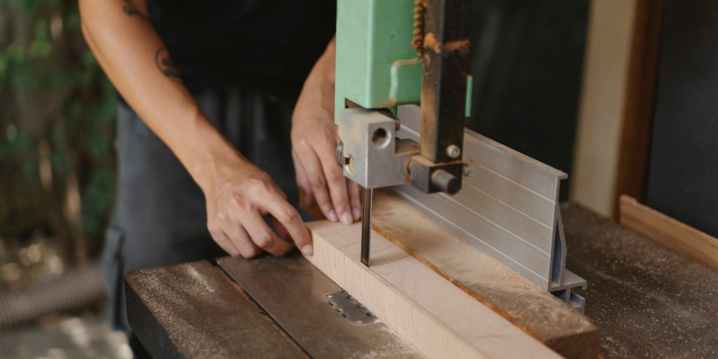 Faceless carpenter cutting timber with band saw on table