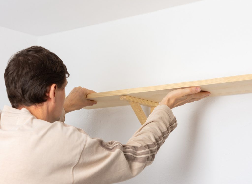 Man hanging up a wooden wall shelf