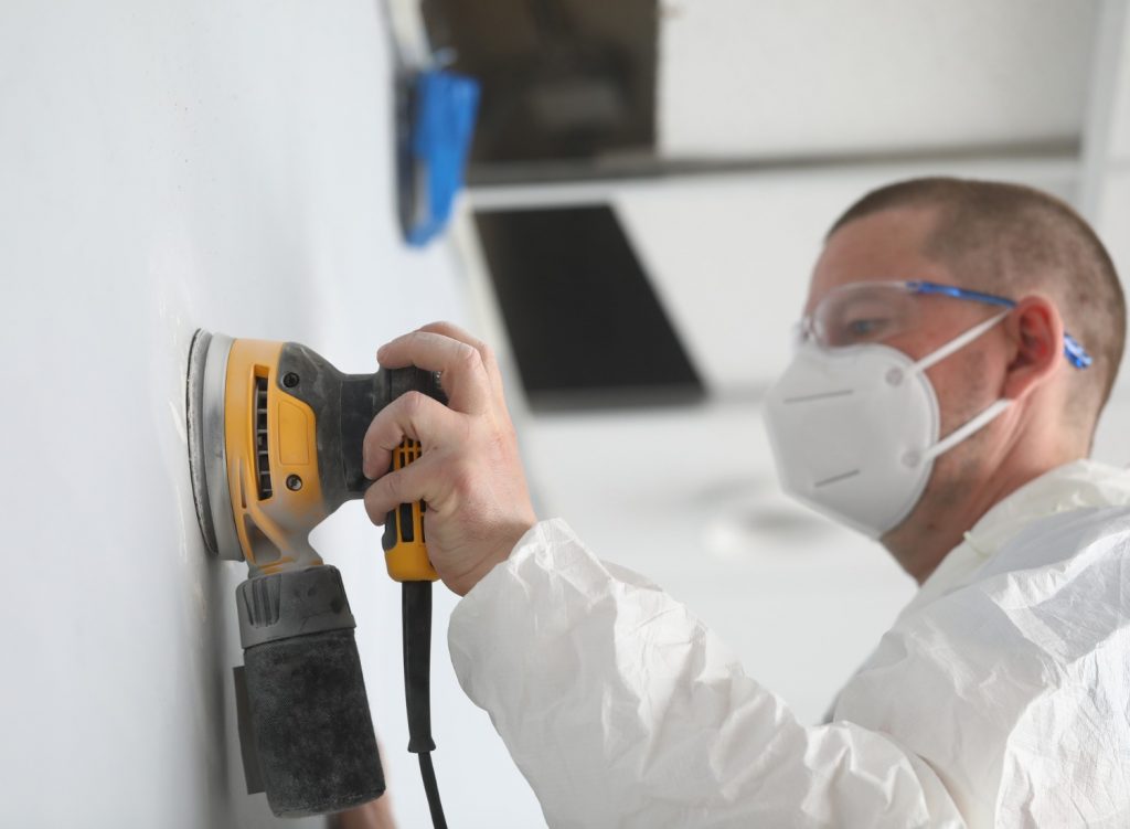 Man sanding a wall and wearing PPE