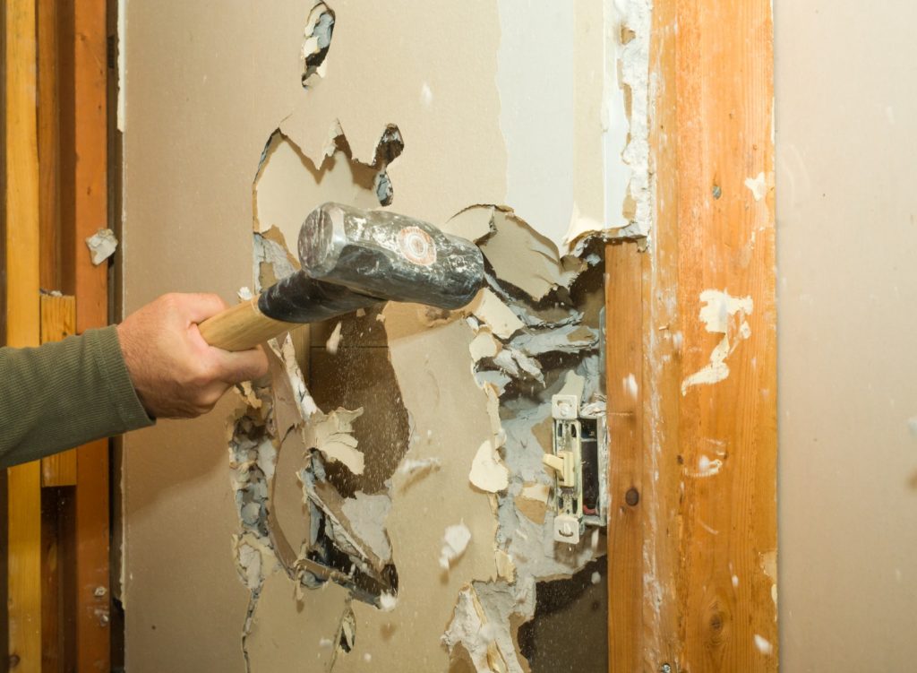 Man demolishing drywall with sledgehammer